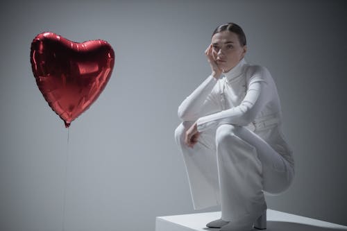 Woman in White Long Sleeve Shirt Beside a Heart Balloon