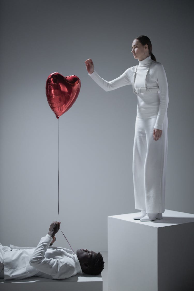 A Woman In White Long Sleeves Popping The Balloon