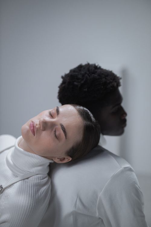 Free Peaceful portrait of a black man and white woman leaning against each other, eyes closed, in white clothing. Stock Photo