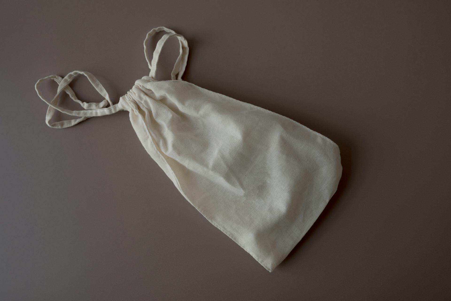 Minimalist soft fabric bag with drawstring on a neutral gray background, ideal for eco-friendly themes.