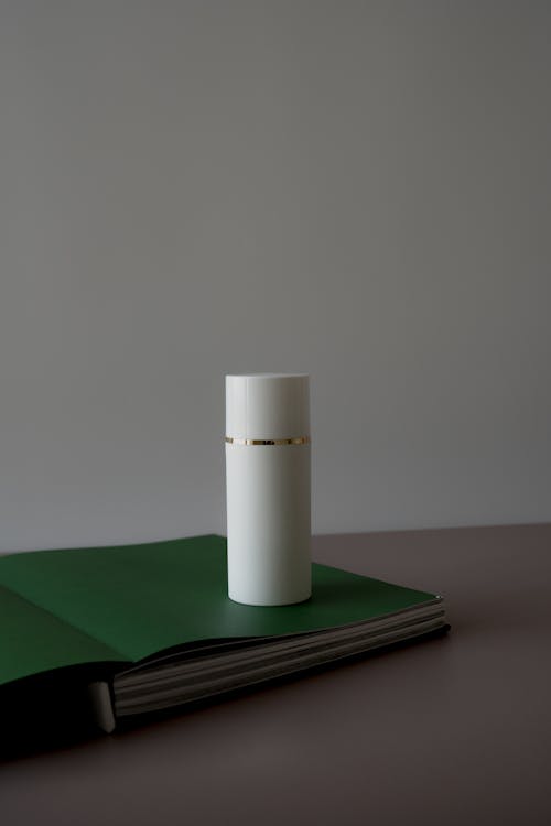 White Cylindrical Container on Green Book
