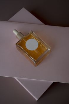 Stylish glass dropper bottle with golden liquid on a soft pink backdrop, ideal for beauty themes.