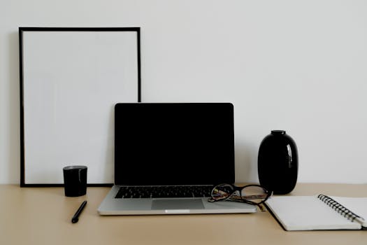 A sleek and organized workspace with a laptop, eyeglasses, and stationery on a tidy desk.
