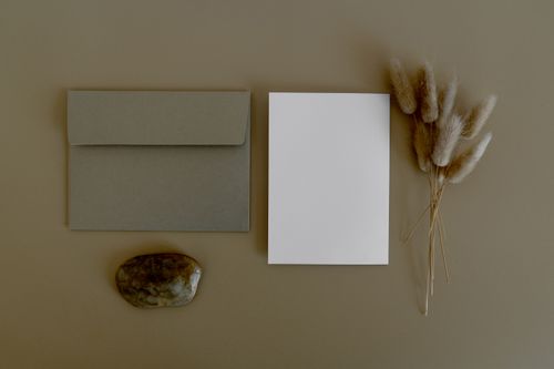 Free Simple flat lay featuring an envelope, blank card, stone, and dried flowers on a brown background. Stock Photo