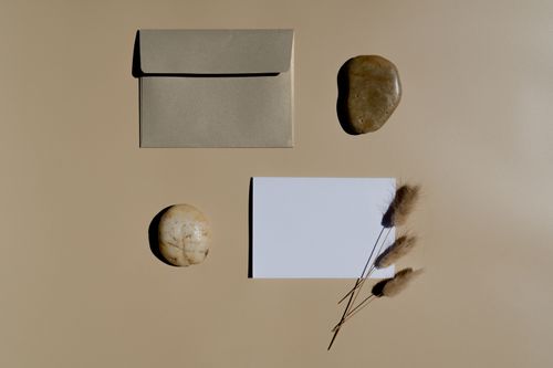Free Minimalist flat lay featuring a brown envelope, white card, stones, and dried grass on a neutral background. Stock Photo