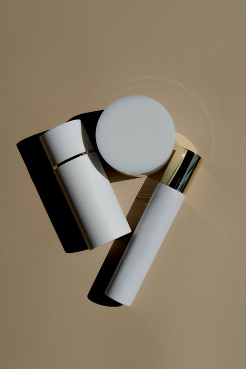 Two White Cylinder Tubes Beside White Jar on Beige Background