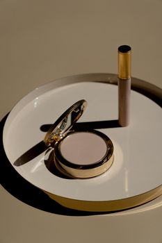 Golden makeup compact with matching mascara on beige tray, representing luxury cosmetics.