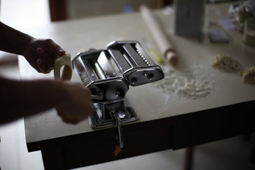 Close-up of a person using a hand crank pasta maker in a kitchen setting.