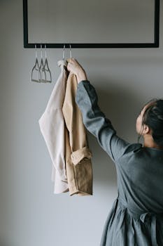 A woman arranges coats on a clothes rack indoors. Minimalist style.