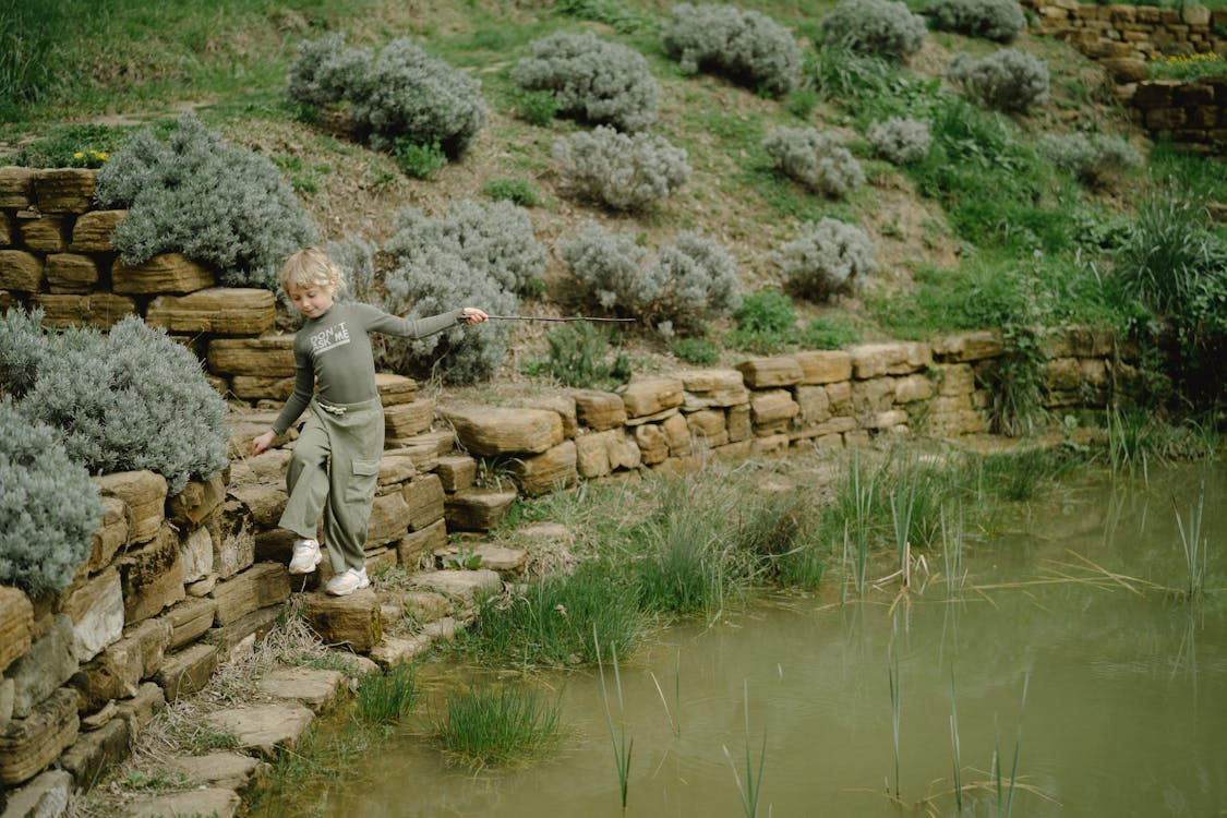 A Kid Walking on Rocks Besides the Pond