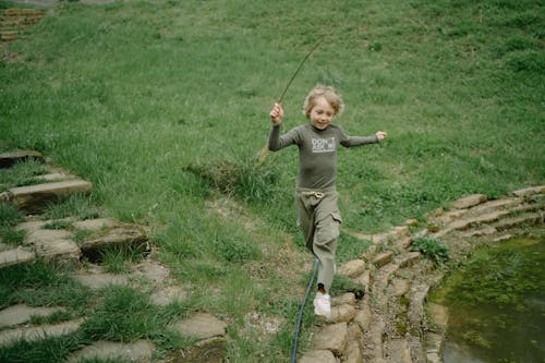 Boy in Gray Long Sleeve Shirt Running on Green Grass Field