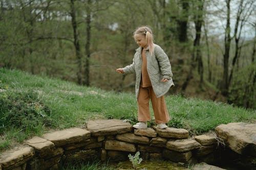 Girl in Gray Jacket and Brown Pants Walking on Brown Rocks