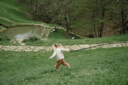 A Girl in White Sweater Running on the Grass Field