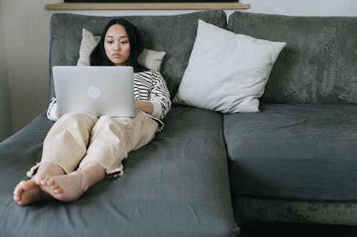 Woman Lying on Sofa while Using a Laptop