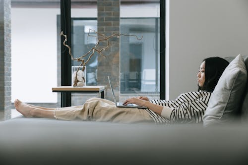 Woman Lying on Couch while Using a Laptop