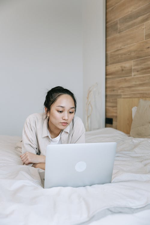 Free Woman Lying on a Bed while Using a Laptop Stock Photo
