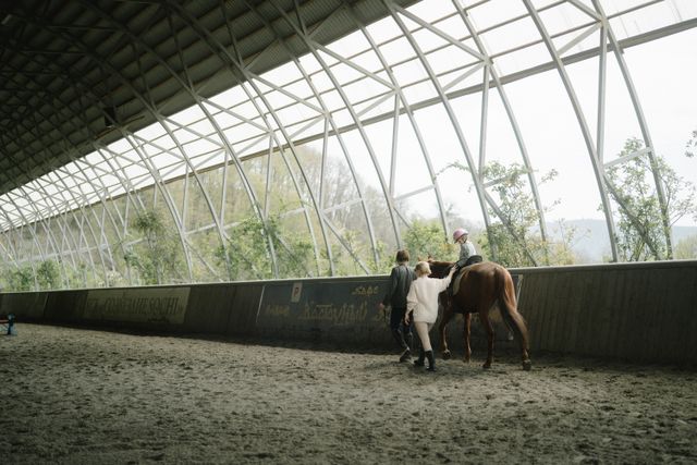 Enfant guidé par deux adultes lors d'un cours d'équitation dans un manège couvert