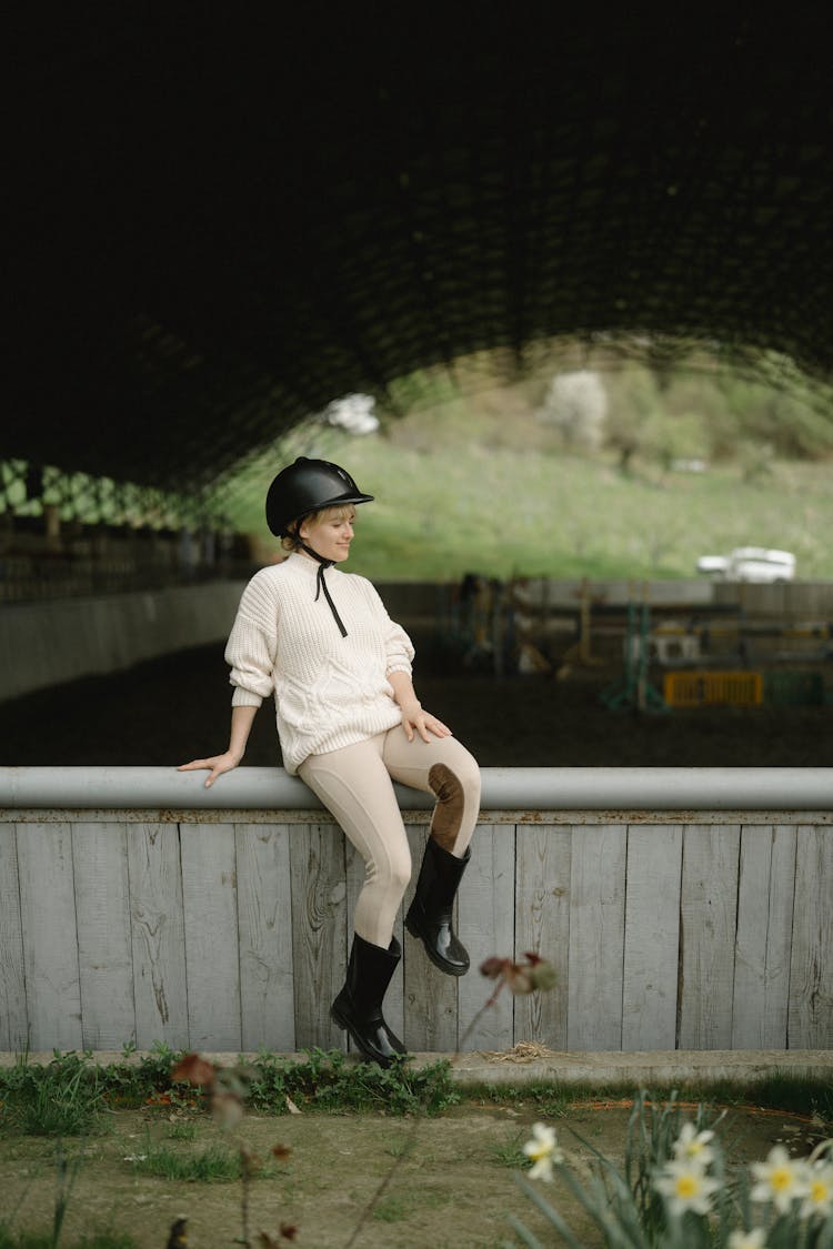 A Woman In Knitted Sweater Sitting On A Metal Fence In A Farm