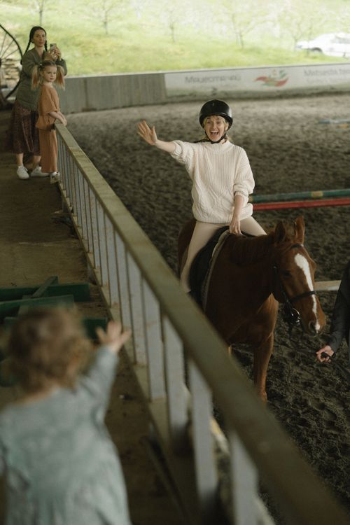 Free Joyful child waves while riding a horse indoors, wearing a helmet for safety. Stock Photo