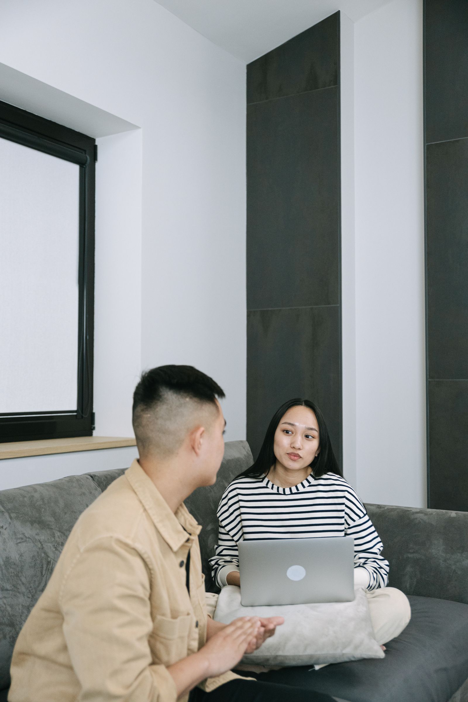 Two people talking on a sofa with a laptop nearby