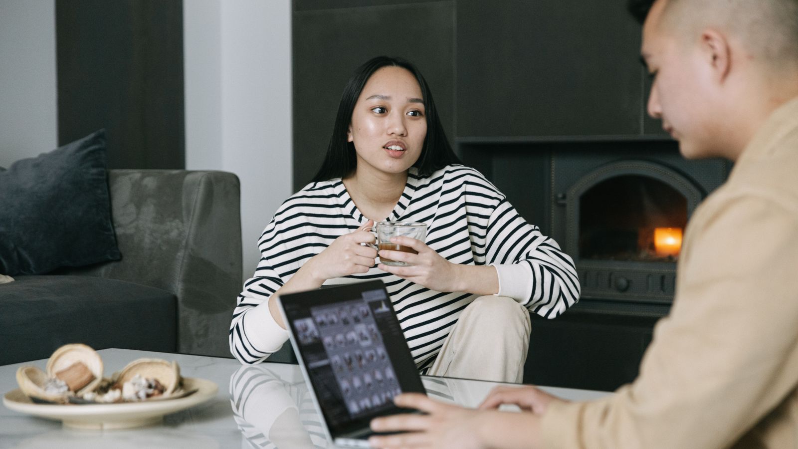 Two adults talking with coffee beside a fireplace