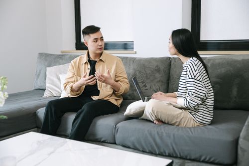 Free Two young adults engaged in a conversation, sitting on a couch at home. Stock Photo