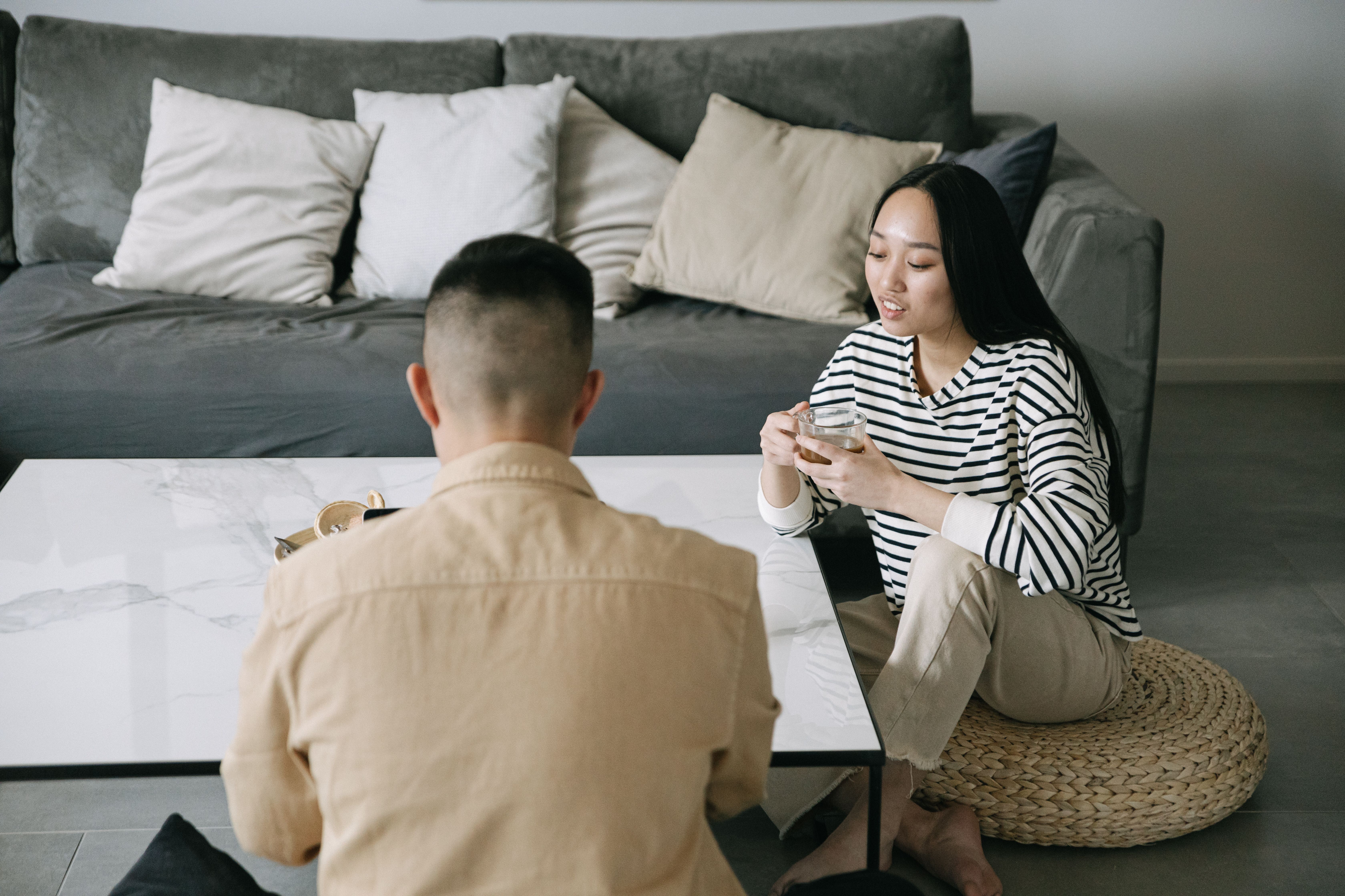 Asian couple having a relaxed conversation at home while enjoying coffee in a modern living room.