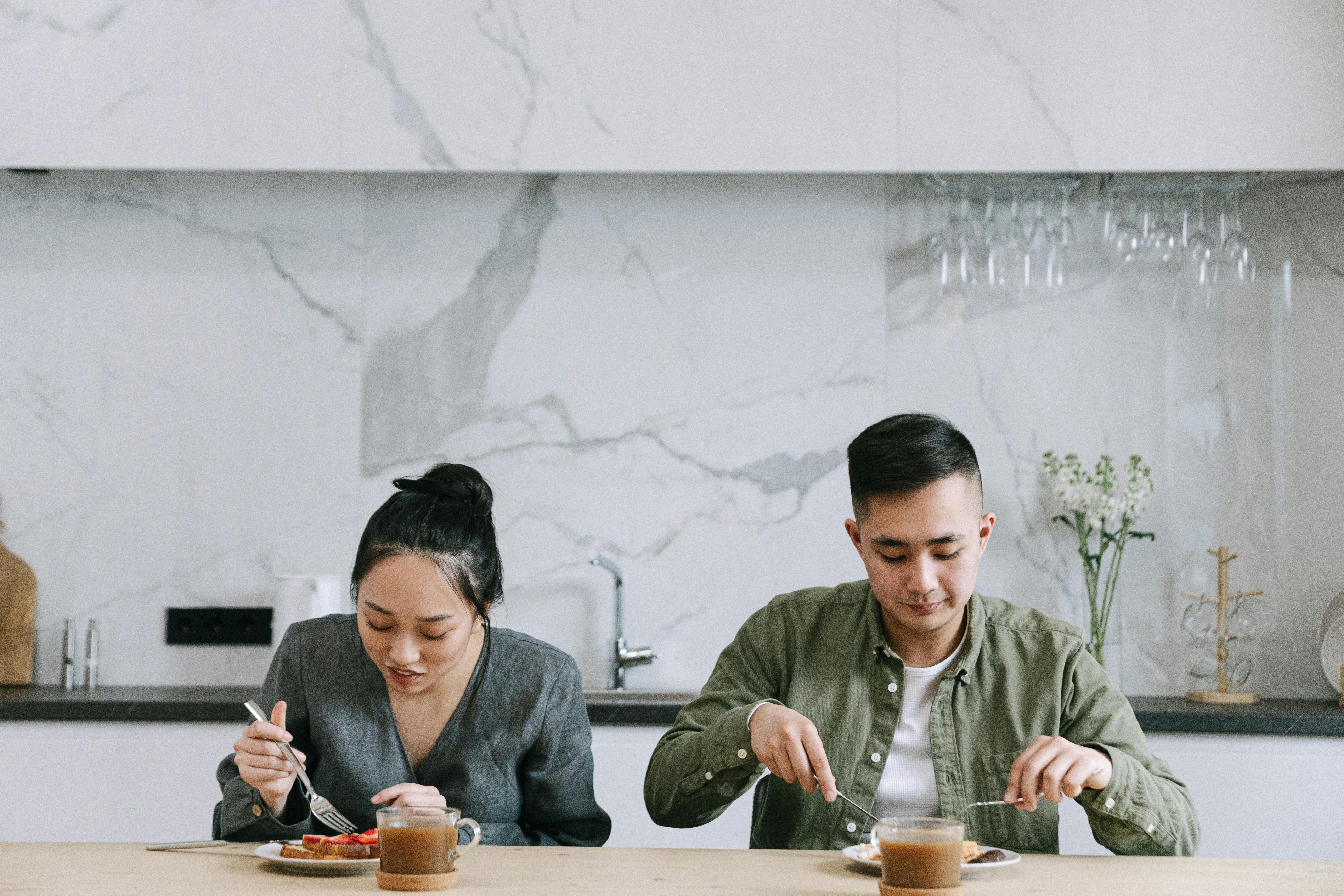 A couple enjoying a meal at a wooden table in a stylish, modern kitchen environment.