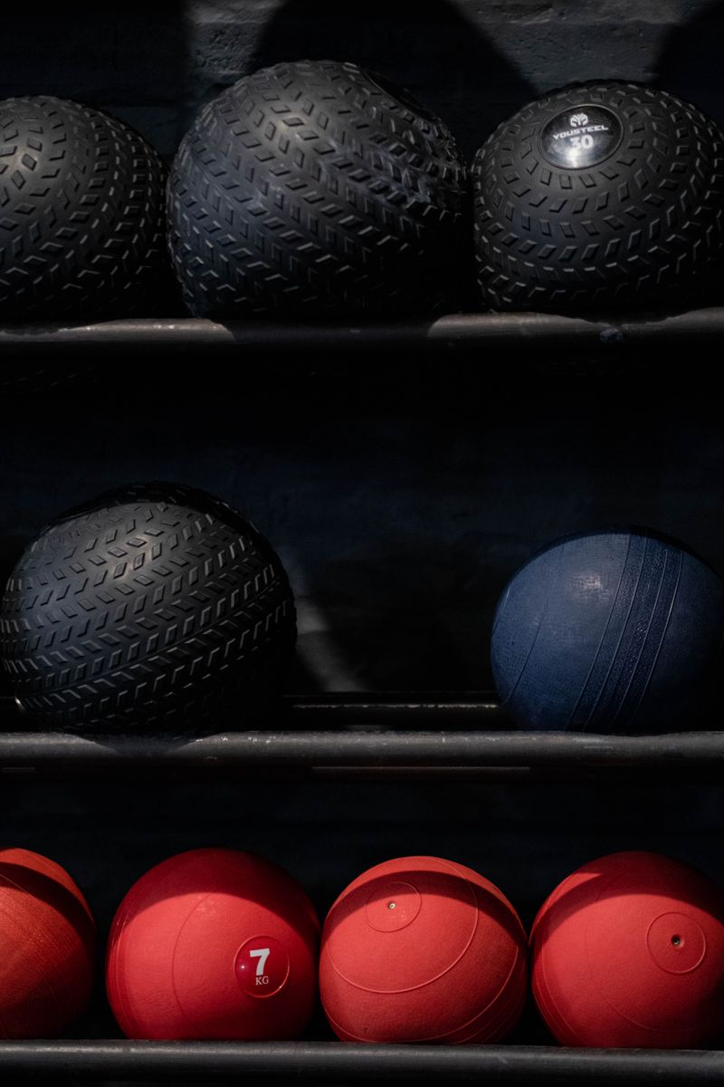 Array of black, blue, and red exercise balls neatly arranged in a gym setting.