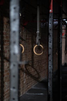 Close-up of gymnastics rings hanging in a dimly lit gym with brick wall background.