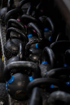 Rows of black kettlebells with blue accents on a gym rack, emphasizing strength training.