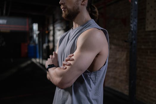 Confident man in a gray tank top standing cross‑armed in a gym setting.