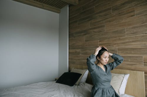 A Woman Fixing Hair While Sitting on a Bed
