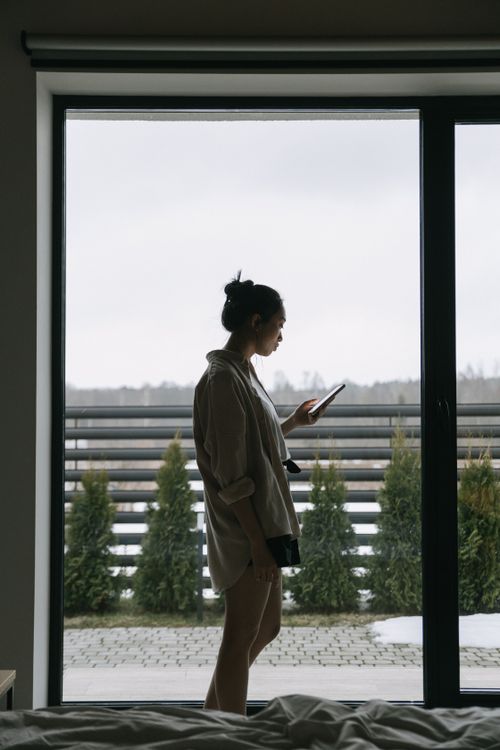 Free Silhouette of woman using smartphone near window with outdoor view. Stock Photo