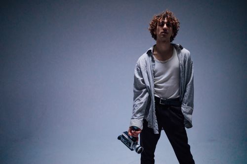 Free Stylish young man with curly hair poses in a studio holding a vintage camera. Stock Photo