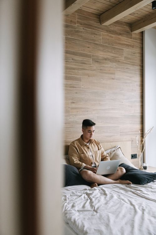Free A young man using a laptop for remote work in a modern, minimalist bedroom setting. Stock Photo