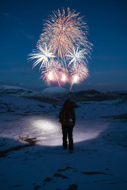 Person Stands on Snow Covered Mountain Looking at Fireworks