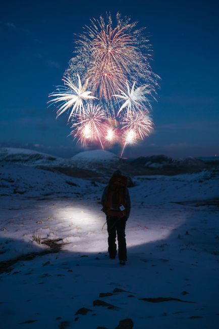 A lone hiker watches fireworks illuminating a snowy winter night, creating a magical outdoor scene.