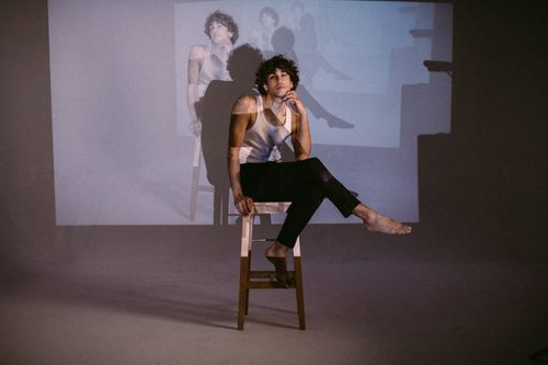 Free A man with curly hair poses on a stool in a studio with projected images and shadows. Stock Photo