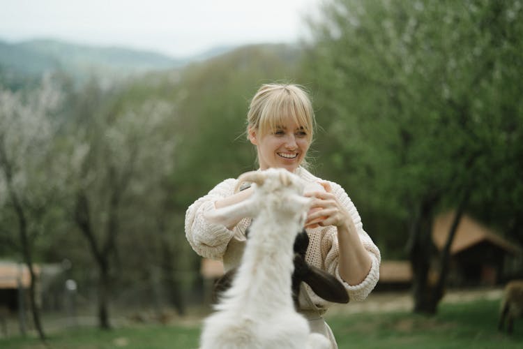 Woman In White Knitted Sweater Standing Beside White Animal