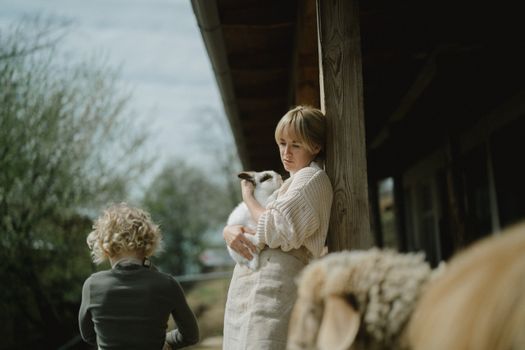 A serene moment captured of a woman cuddling a rabbit outdoors on a farm porch.