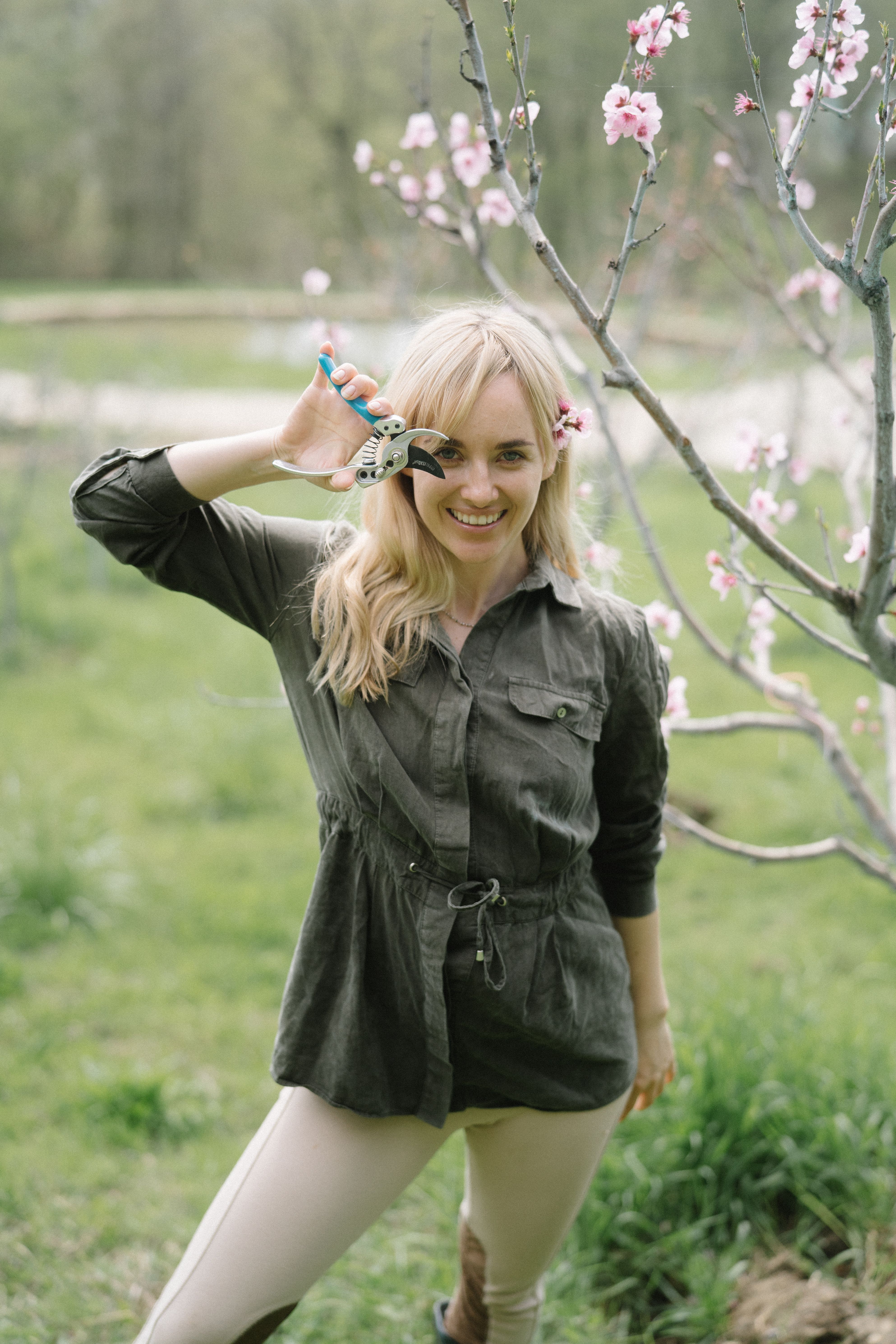 Smiling woman with pruner among cherry blossoms, showcasing spring gardening.
