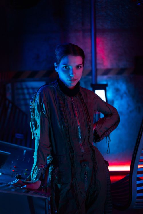 Free A woman in a futuristic space suit poses with neon lights creating a sci-fi atmosphere. Stock Photo