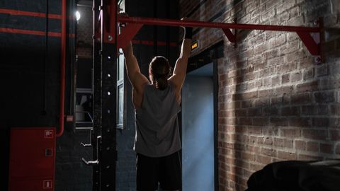 Man in activewear doing pull-ups in an indoor gym setting, emphasizing fitness and well-being.