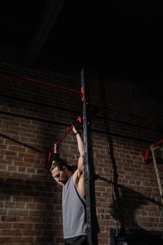 A man in a gym performing a pull-up exercise against a brick wall.