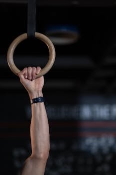 Close-up of an adult's hand firmly grasping a gymnastic ring in a gym setting.