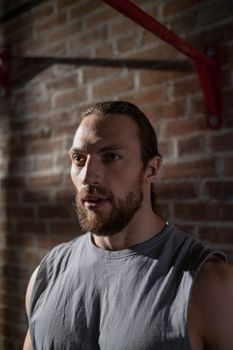Portrait of an athletic man with a beard in a dimly lit rustic interiors, conveying contemplation.