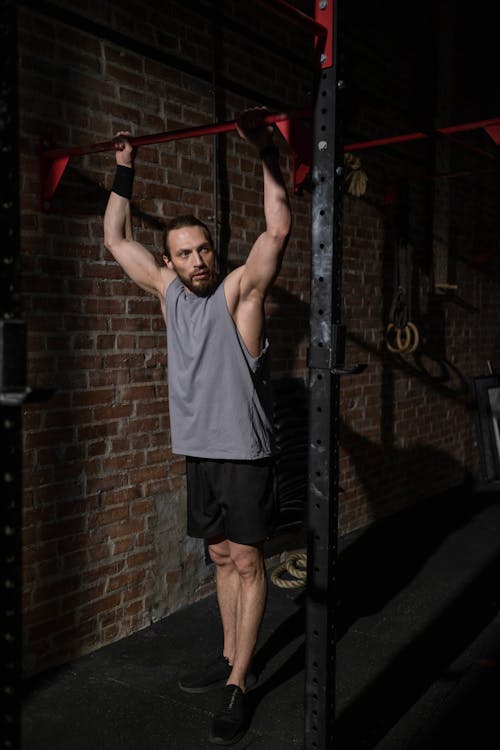 Free Man in Gray Tank Top Holding onto a Pull-Up Bar Stock Photo