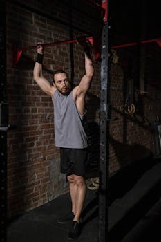 Man in gym gear performing pull-up exercise on a bar indoors, depicting strength and fitness.