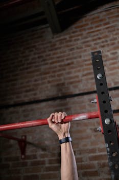 Close-up of a hand gripping a pull-up bar inside a gym with brick wall background.